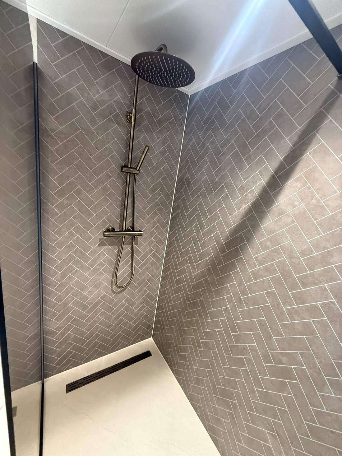 Douche met visgraattegels en gouden regendouche