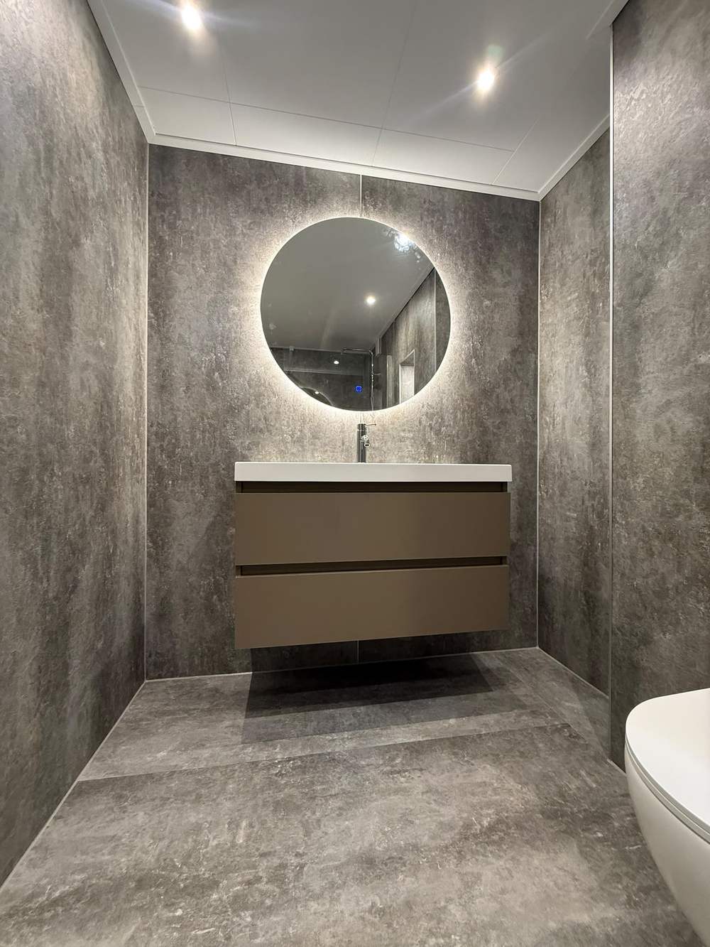 Betonlook badkamer met houten meubel en ronde spiegel