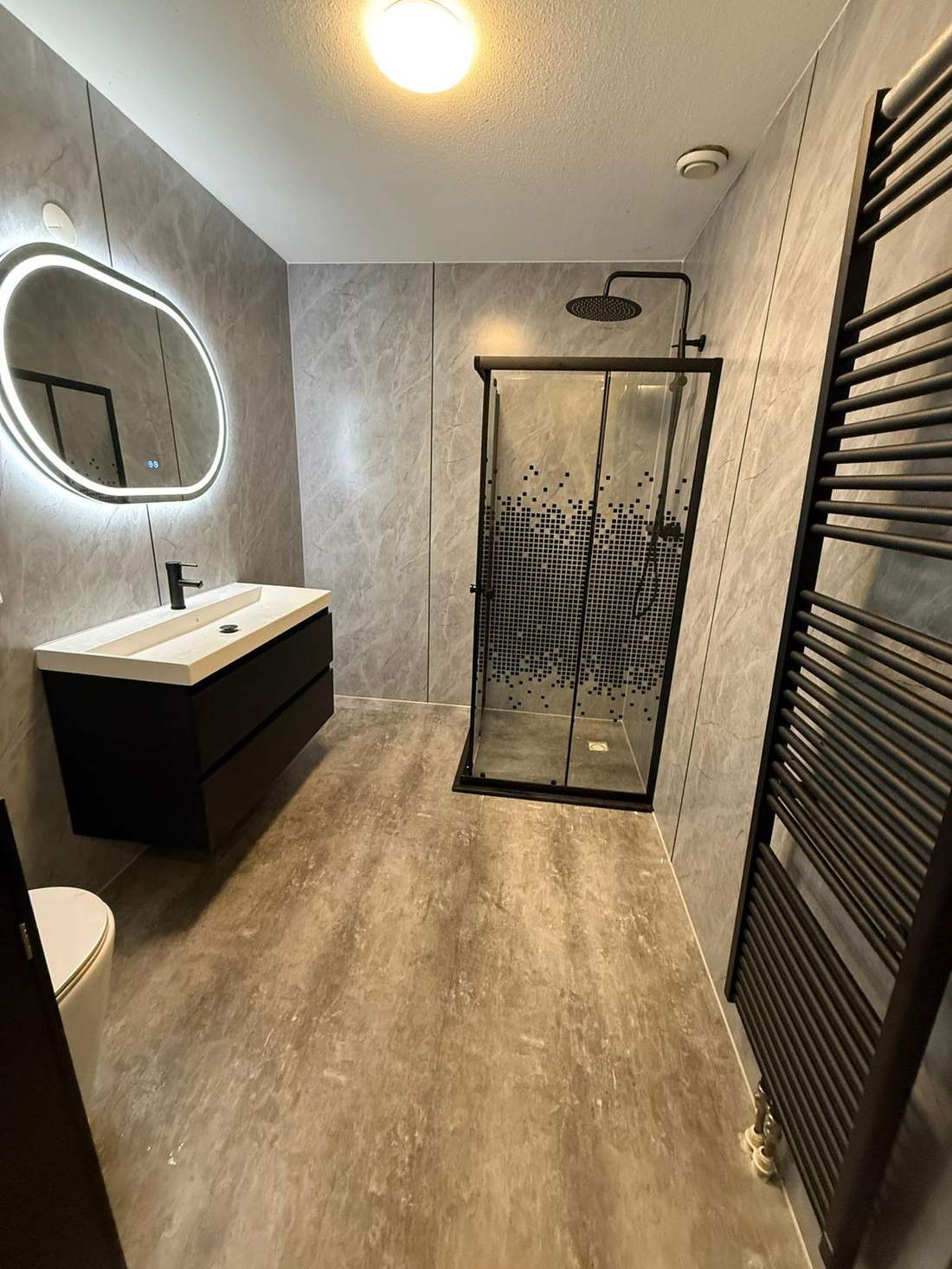 Vernieuwde badkamer met marmerlook wandpanelen en zwart douchescherm